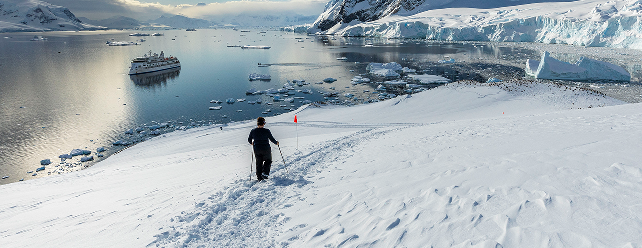 A person hiking down a snowy hill in front of the Sylvia Earle ship